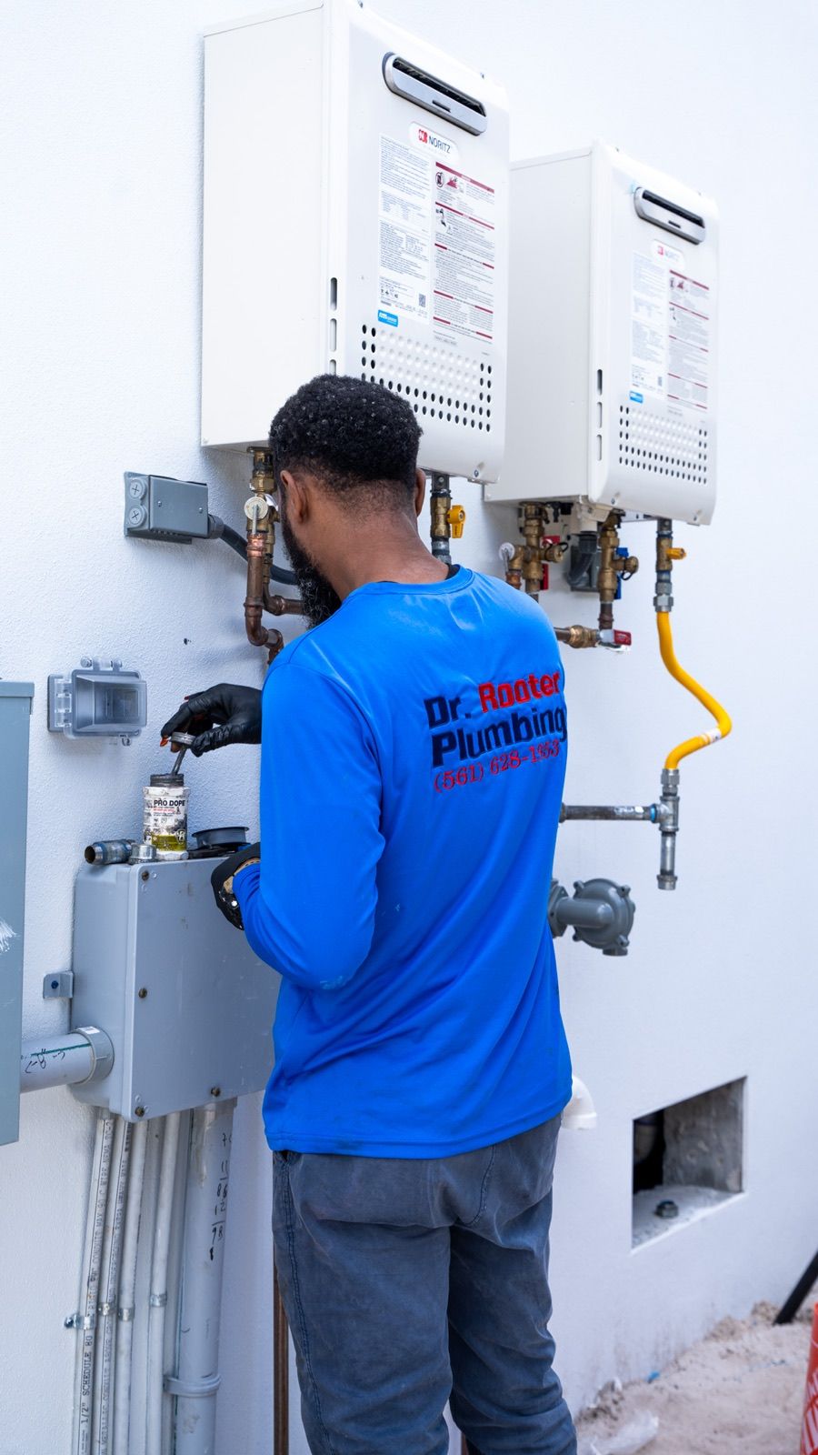 Dr. Rooter Plumbing technician connecting the gas and water lines under two tankless water heaters